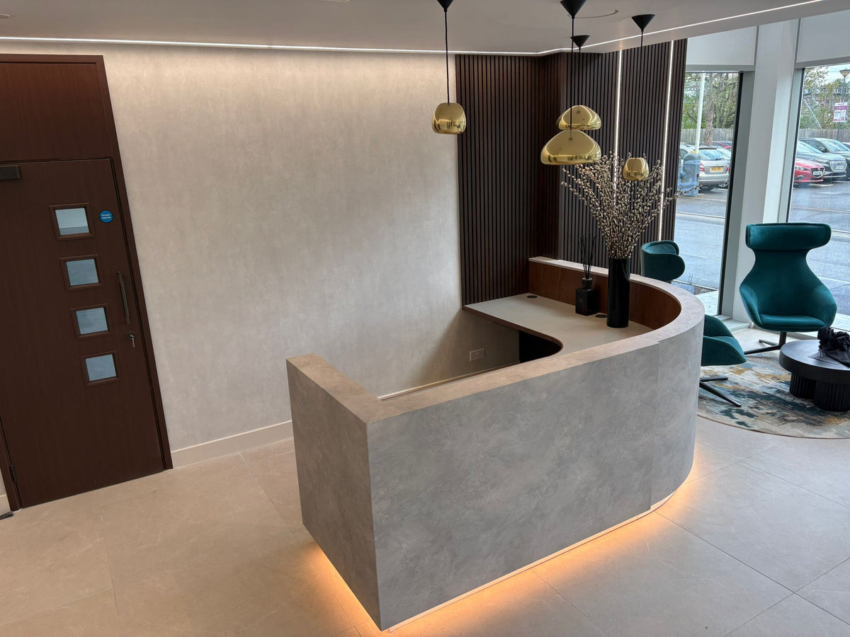 Curved reception desk with a concrete-effect front, dark timber backdrop and pendant lighting