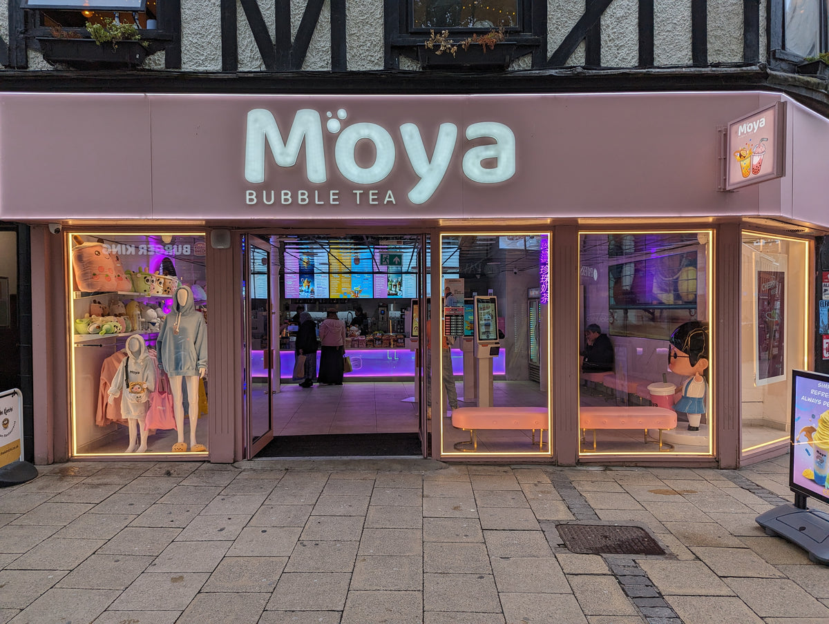 Illuminated Moya shopfront sign photographed at night