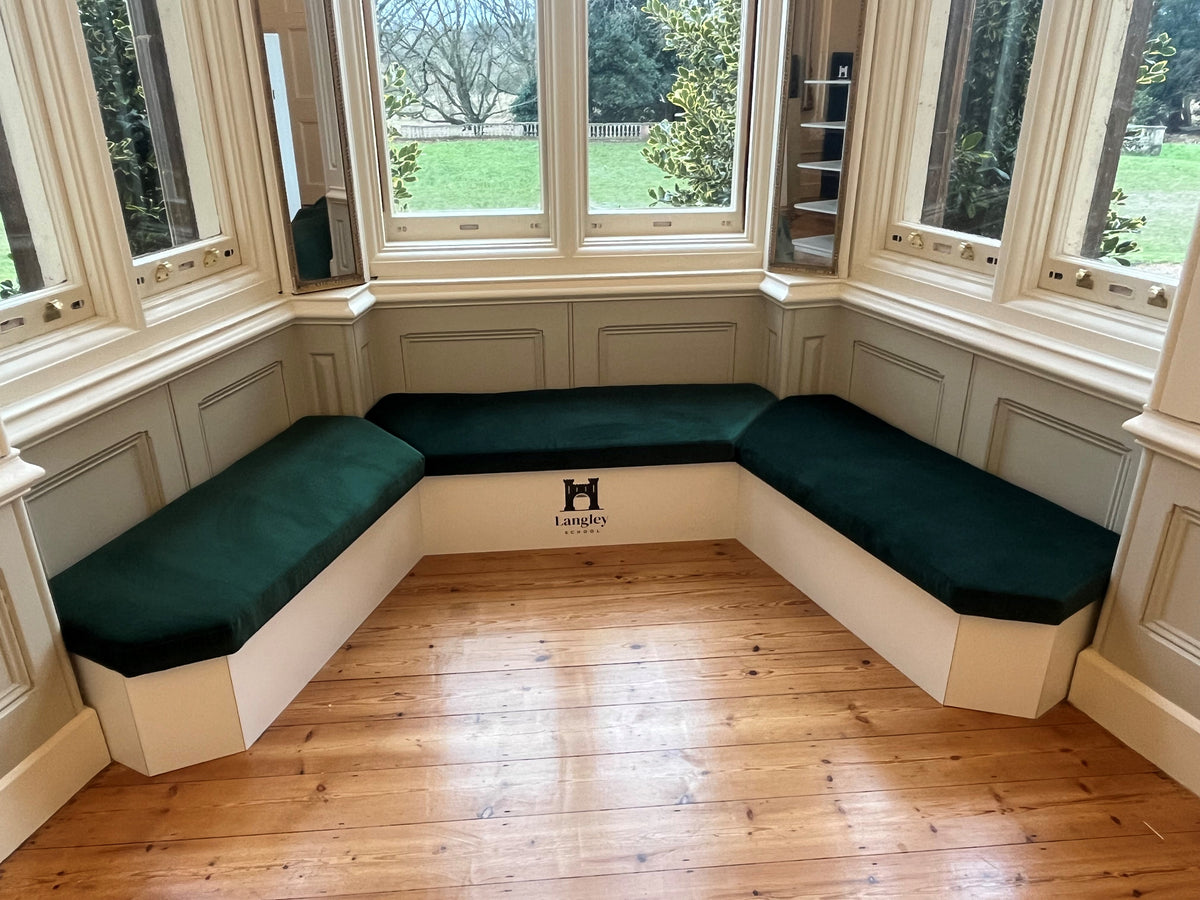 Fitted white window seat with a green cushion in a library interior